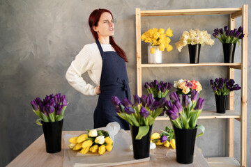 Young caucasian saleswoman girl standing and suffering from back pain while working, standing by the window display in a flower shop.