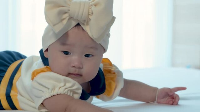 4K 25fps Slow Motion,  Close-up of a newborn girl, Asian, 5 months old, just woke up from sleep. was lying on the bed and looking for her mother, on her head tied in a large bow with a yellow cloth.