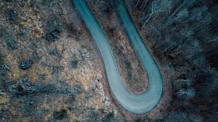 Aerial high angle view of narrow winding curvy mountain road among the trees in winter forest. Bird's eye view landscape.