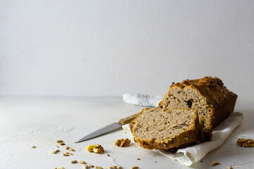 Homemade bread with seeds on a light napkin. A knife in the background. Slices of bread, seeds and nuts on the table. Light background, space for text
