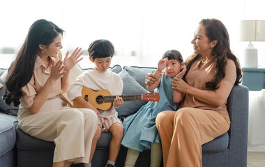 Happy Asian family with grandmother playing guitar and singing a song together at home.