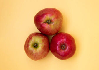Three red apples are lying on a yellow background