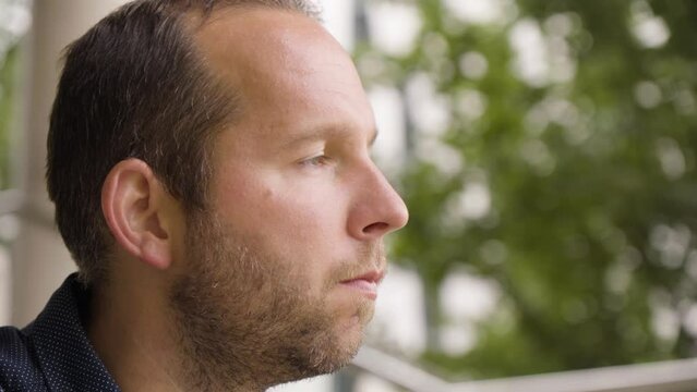 A Caucasian man thinks about something in an urban area - face closeup