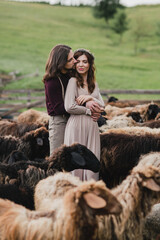 Romantic, young and happy caucasian couple in stylish clothes traveling together on the sheep farm in beautiful nature. Love, relationships, romance, animal care, happiness concept.