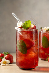 Refreshing strawberry summer drink in glass with ice cubes and mint leaves.