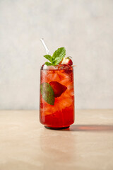 Refreshing strawberry summer drink in glass with ice cubes and mint leaves.