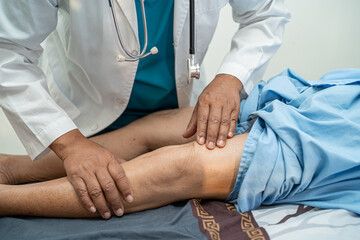 Asian doctor physiotherapist examining, massaging and treatment knee and leg of senior patient in...