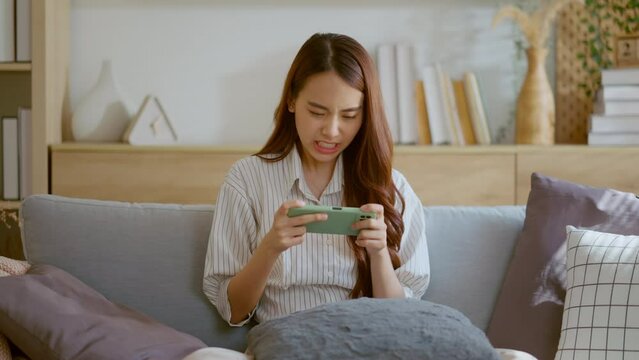 happiness asian young female enjoy playing and competition game smartphone mobile online on sofa in living room home interior background,asia woman esport playing game streaming home isolate ideas