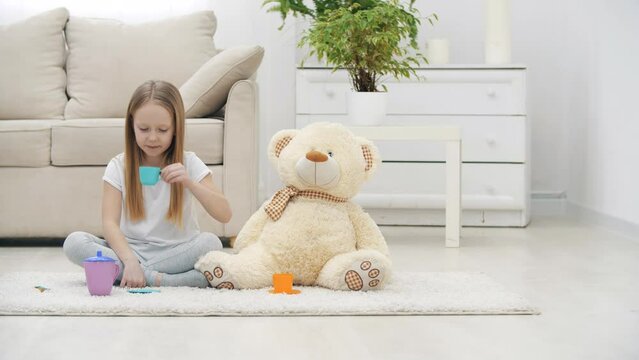 4k slowmotion video of little girl playing with teddy bear sitting on the floor.