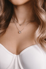 Close up of silver chain and elegant pendant with diamond on the chest of young caucasian tanned blonde woman with wavy hair. Jewelry with gemstones, wedding holiday accessories for a bride