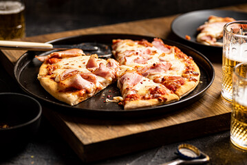 Pizza with bacon, crushed chilli and mozzarella served with beer. Dark background.