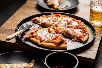 Pizza with bacon, crushed chilli and mozzarella served with beer. Dark background.