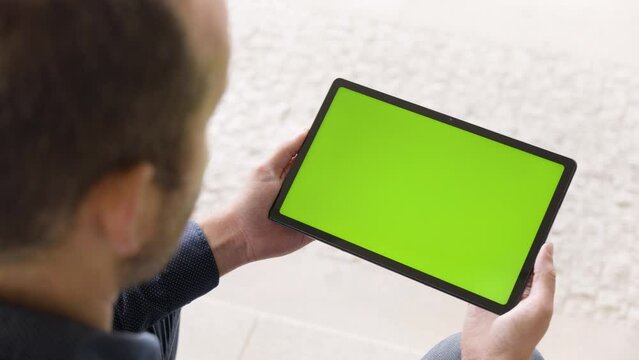 A Man Looks At A Tablet (horizontal) With Green Screen - Closeup From Behind The Shoulder