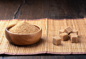 Wooden bowl with cane sugar and sugar cubes on a food mat.