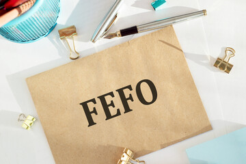 The word FEFO - abbreviation of first expired first out on crafted envelope lying on the desk with office tools.