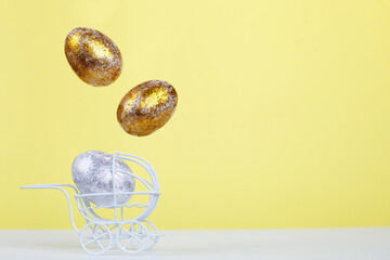 Easter golden and silver eggs levitation in the white baby stroller on a yellow background. Newborn concept