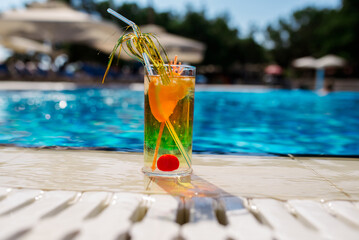 Glass of orange juice welcome drink at infinity swimming pool with ocean background. cocktail with alcohol and without alcohol by the pool with orange and ice. Selective focus.