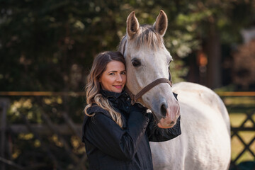 Young woman standing next to white Arabian horse, blurred trees background, closeup detail