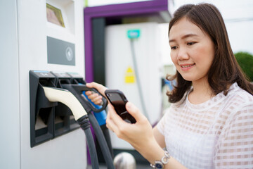 Fototapeta na wymiar Happy Asian woman holding a DC - CCS type 2 EV charging connector at EV charging station.