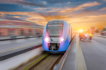 Railway station with modern high speed red commuter train with motion blur effect at colorful beautiful sunset.
