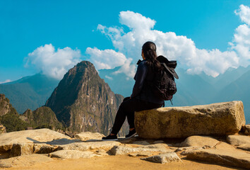Mujer caucásica sentada sobre una roca en el fondo de la antigua ciudad de Machu Picchu.