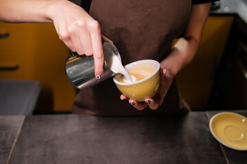 Coffee making process. Barista pouring warm milk into coffee cup.