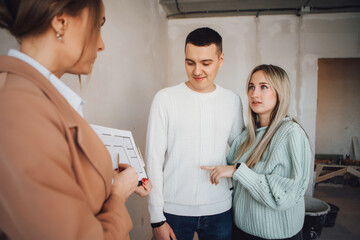 Real estate agent showing condo for sale to young couple. Female designer or realtor show apartment plan