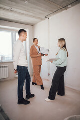 Female designer or realtor show apartment plan. Female designer or realtor show new apartment in unfinished building to man and woman