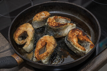 The cook fries carp fish in a frying pan on an induction stove