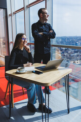Young business woman behind a laptop wearing glasses sitting at a table having a corporate business meeting with colleagues in a modern office. Business career concept. Free space, selective focus