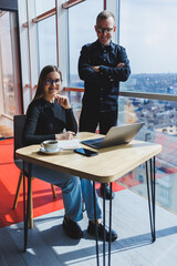 Young business woman behind a laptop wearing glasses sitting at a table having a corporate business meeting with colleagues in a modern office. Business career concept. Free space, selective focus