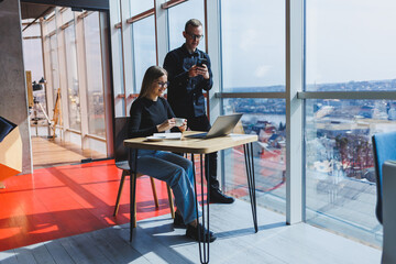 Young business woman behind a laptop wearing glasses sitting at a table having a corporate business meeting with colleagues in a modern office. Business career concept. Free space, selective focus