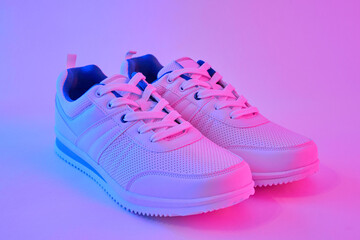 Fashion white sneakers in neon light. Sport shoes for training in the gym. Creative minimalism. 90s concept.