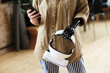 Close-up of woman with prosthetic arm using her mobile phone to connect virtual reality goggles...