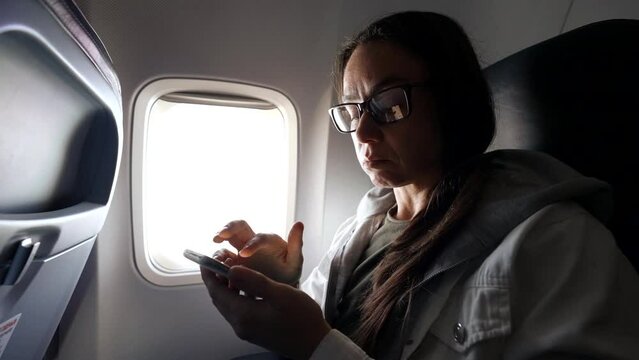 female passenger in cabin of airplane, using smartphone, switching on plane mode in mobile phone