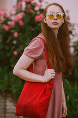 Young beautiful red-haired long-haired woman in a summer pink dress walks through the streets of a summer city.