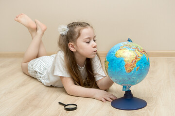 little girl lies on the floor and carefully examines the globe