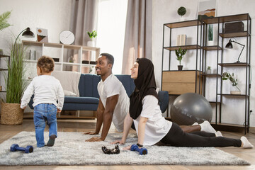 25-30 age beautiful sporty couple practicing yoga doing four-limbed staff pose at home. Muscular Athletic African Man and Beautiful Muslim Fitness Woman in Workout Clothes Doing Push Up Exercises.