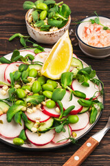 Fresh spring salad plate with radish, cucumber, green pea, sunflower, soy and mung bean sprouts, edamame and flax seeds. Vegetarian vegan healthy food. Top view, wooden kitchen table