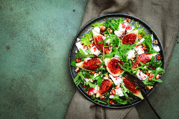 Delicious summer salad with figs, feta cheese, walnuts, arugula and sweet  jam dressing on rusty green table background, top view, negative space