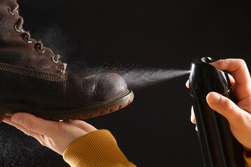 A woman applies the spray to brown nubuck women's winter boots. Water-repellent care for shoes,...