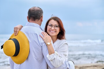 Portrait of happy hugging middle age couple, sea nature sky waves background.