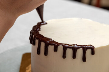 Applying streaks of chocolate glaze with a pastry bag on the cake. Selective focus. Picture for articles about food, confectioners.