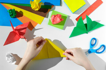 Paper crafts, scissors, colored paper sheets and scraps, on white table. Origami. Children working...