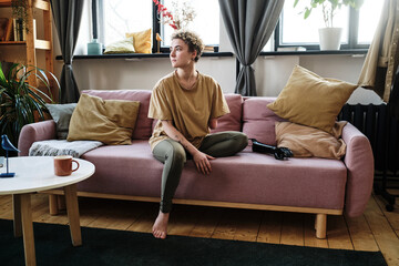 Girl with amputee arm sitting on sofa in the living room with prosthesis, she looking pensive