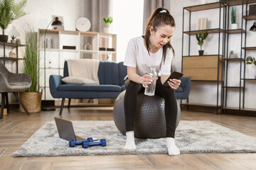 Happy fitness woman training on swiss ball in living room. Portrait of muscular woman enjoying home...