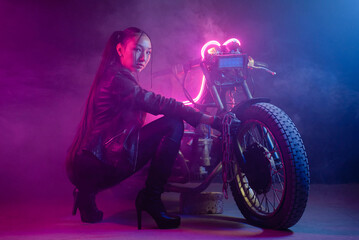 Plakat Girl a motorbiker near the old motorcycle in the neon lights.