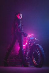 Fototapeta na wymiar Girl a motorbiker near the old motorcycle in the neon lights.