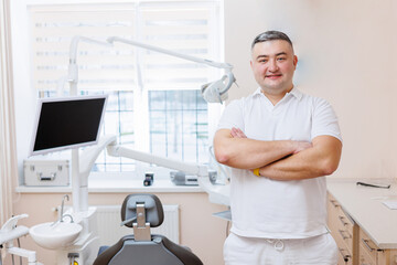 Naklejka na ściany i meble The concept of medicine, profession, dentistry and medicine - a smiling middle-aged dentist on the background of a medical office. The dentist is in his dental office.
