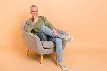 Full size photo of strict old grey hairdo man sit wear eyewear pullover jeans footwear isolated on beige background
